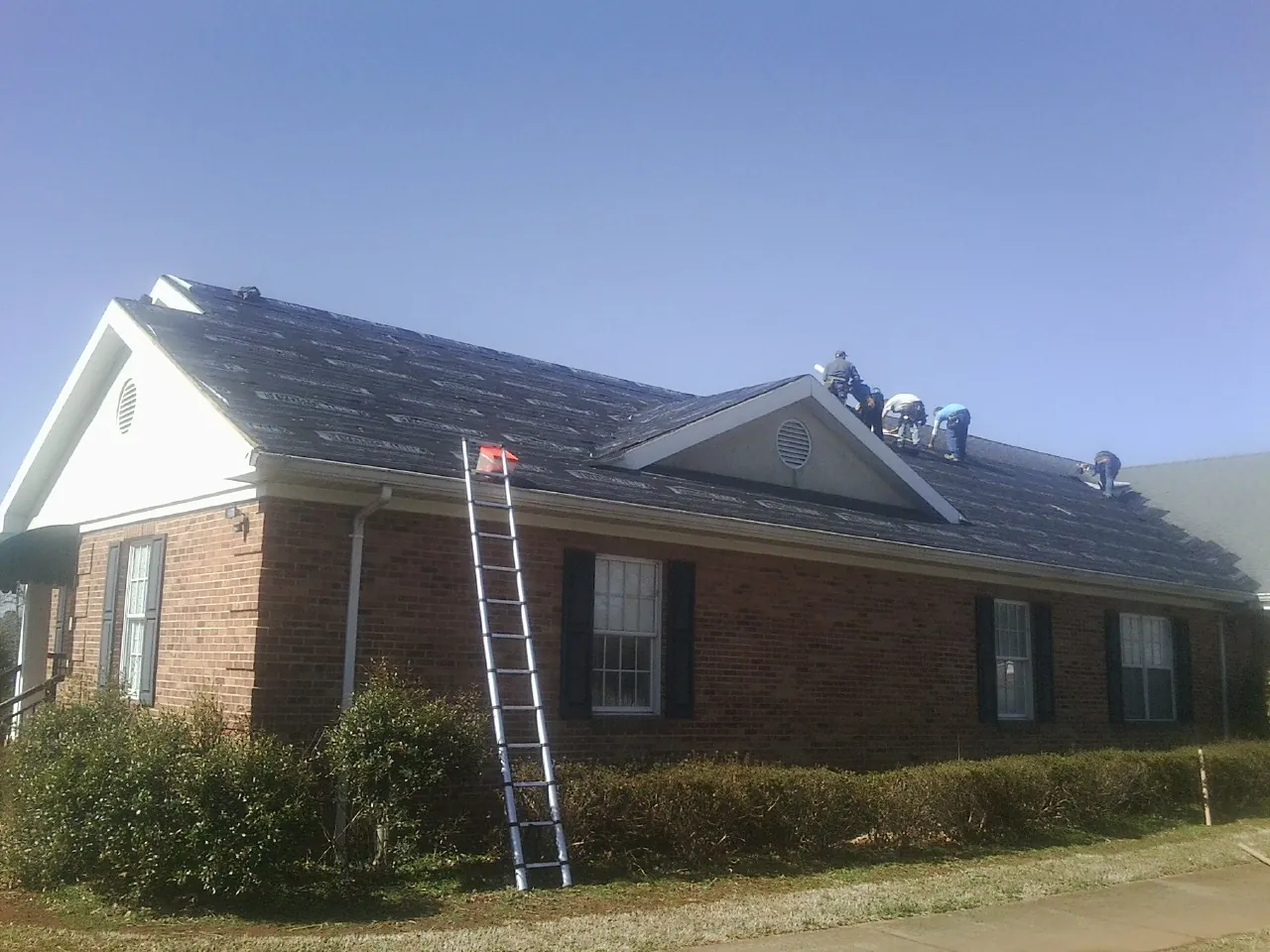 Crew tearing shingles off a brick ranch roof with a ladder set — Emergency Roof Repair work by our crew in Eufaula