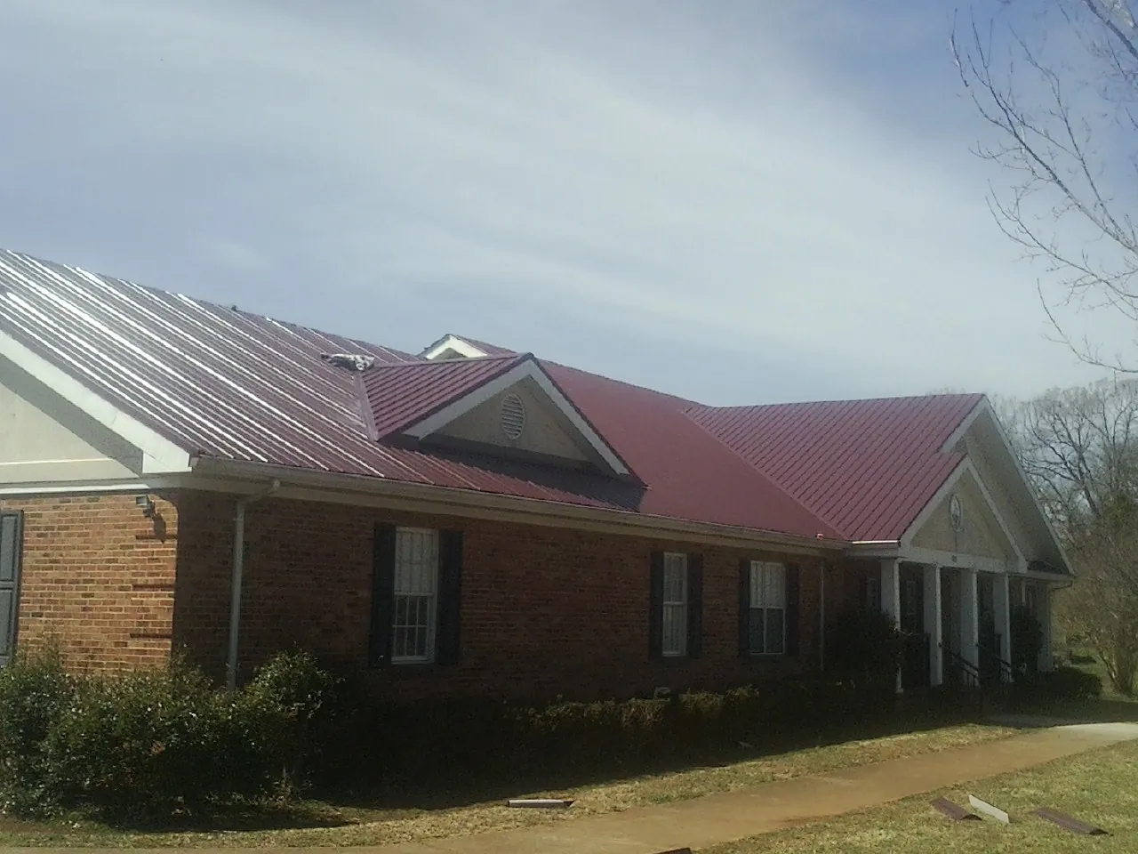 Red metal roof with gabled entries on a long brick building, from a Hail Damage Roof Repair job in Eufaula