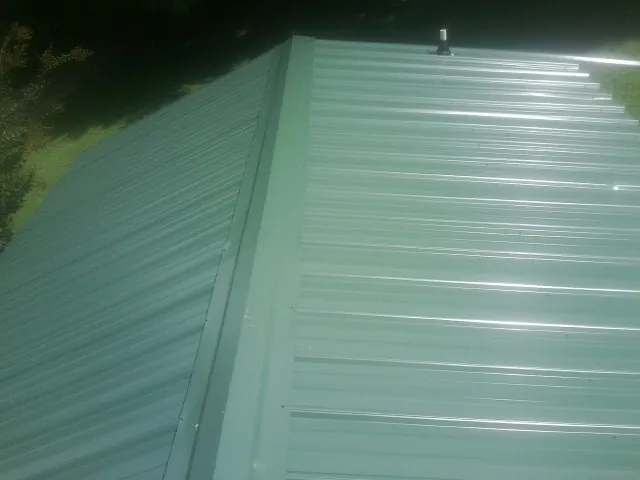 New green metal panels meeting at the ridge of a roof — Flat Roof Repair work by our crew in Eufaula