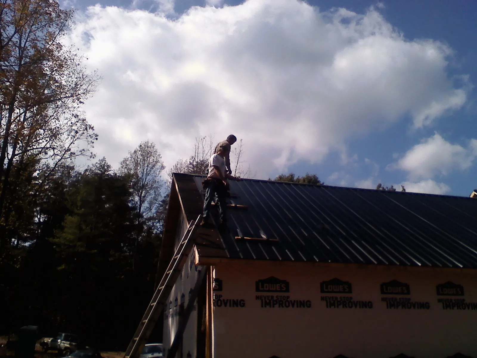 Roofer fastening dark metal panels high against a cloudy sky, from a Roof Inspection job in Eufaula