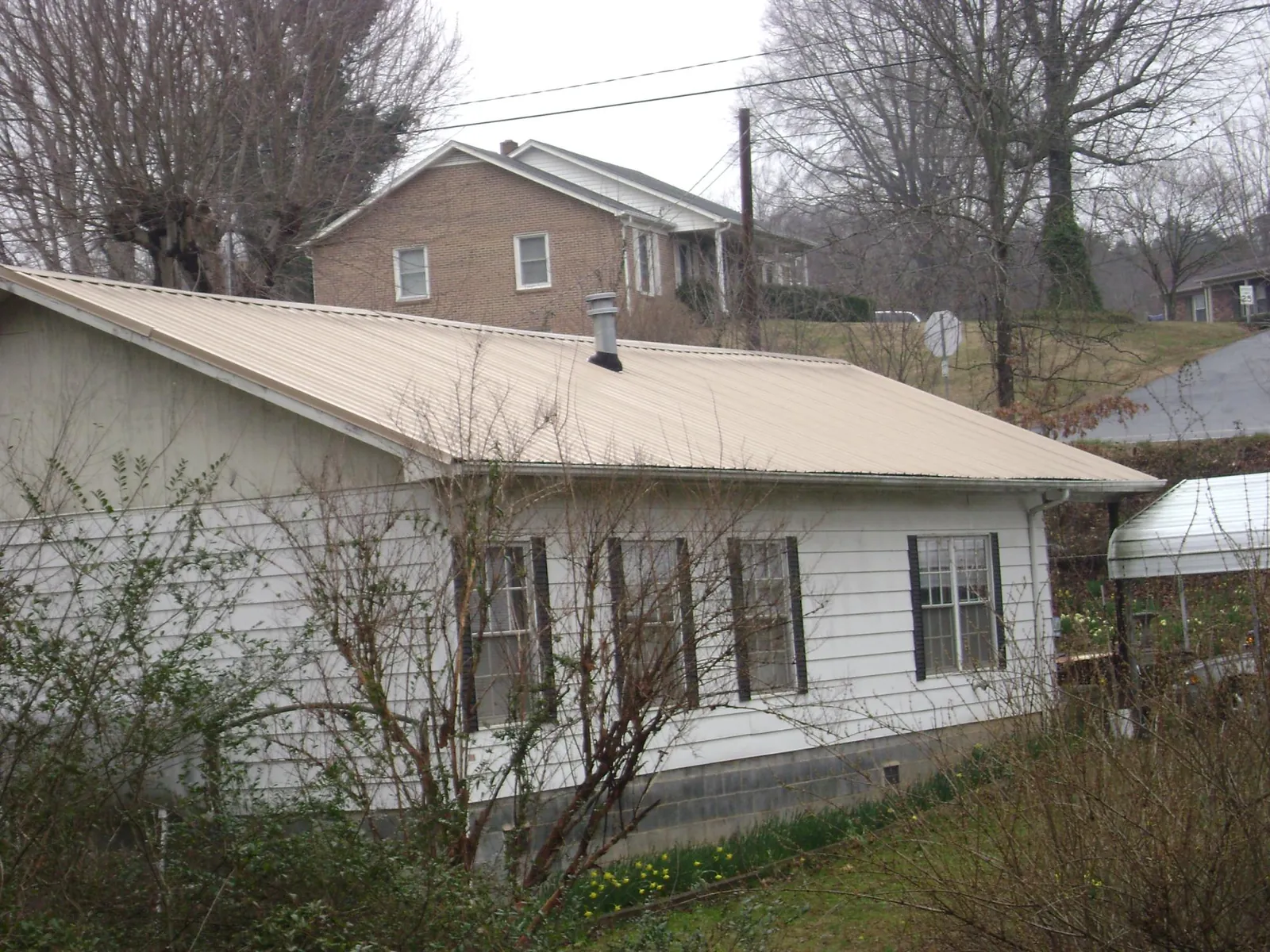 Tan metal roof on a white sided house set into a hillside — Commercial Roofing by Roofing Brothers in Eufaula